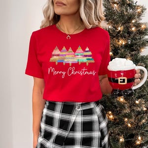 K&ouml;nnte beinhalten: Rotes T-Shirt mit einem Motiv von bunten Weihnachtsb&auml;umen und dem Text "Merry Christmas".