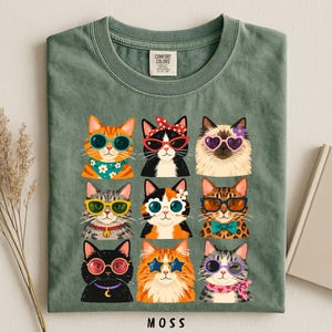 A green t-shirt with a collage of nine cat illustrations wearing sunglasses and accessories, arranged in a grid pattern.