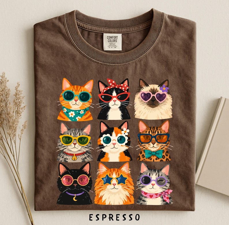 A t-shirt with a graphic design of nine cats wearing sunglasses and accessories, arranged in a 3x3 grid.