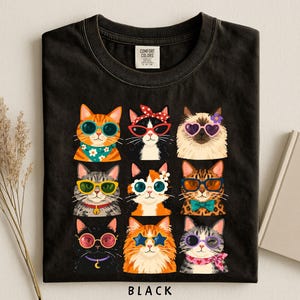 A black t-shirt with a collage of nine cat illustrations wearing sunglasses and accessories, arranged in a 3x3 grid.