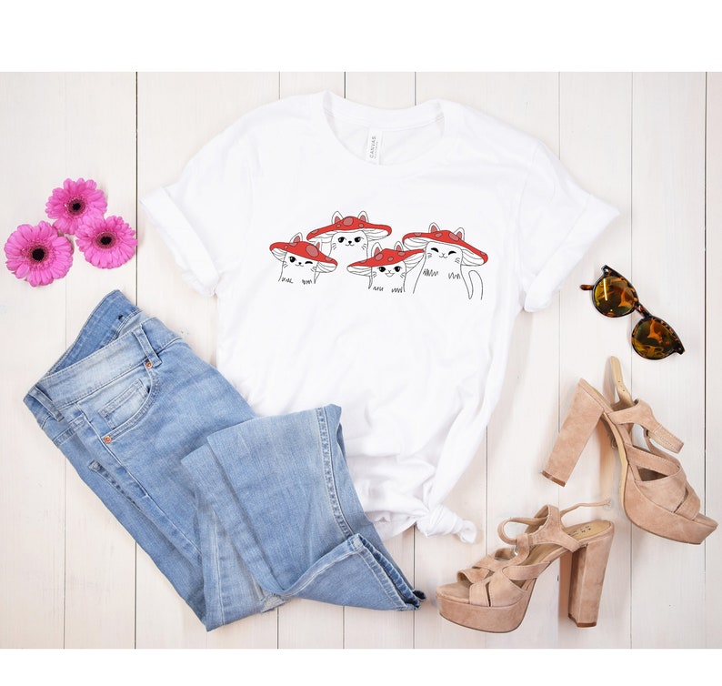 May include: White t-shirt with a graphic of four cats wearing red mushroom hats. The text on the shirt reads "I love you" and "meow meow".