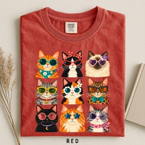 A red t-shirt with a collage of nine cat illustrations wearing sunglasses and accessories, arranged in a 3x3 grid.