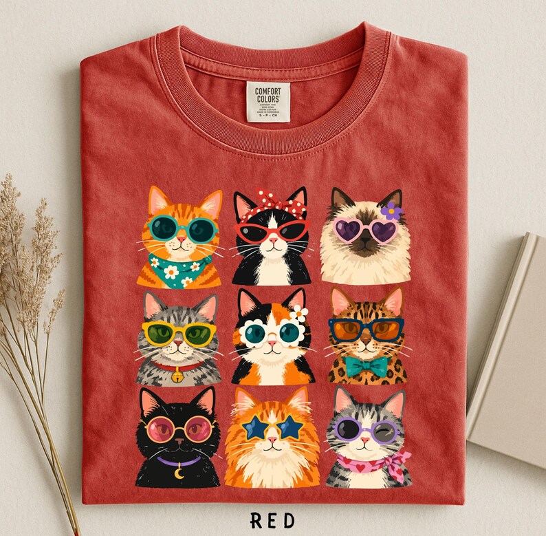A red t-shirt with a collage of nine cat illustrations wearing sunglasses and accessories, arranged in a 3x3 grid.