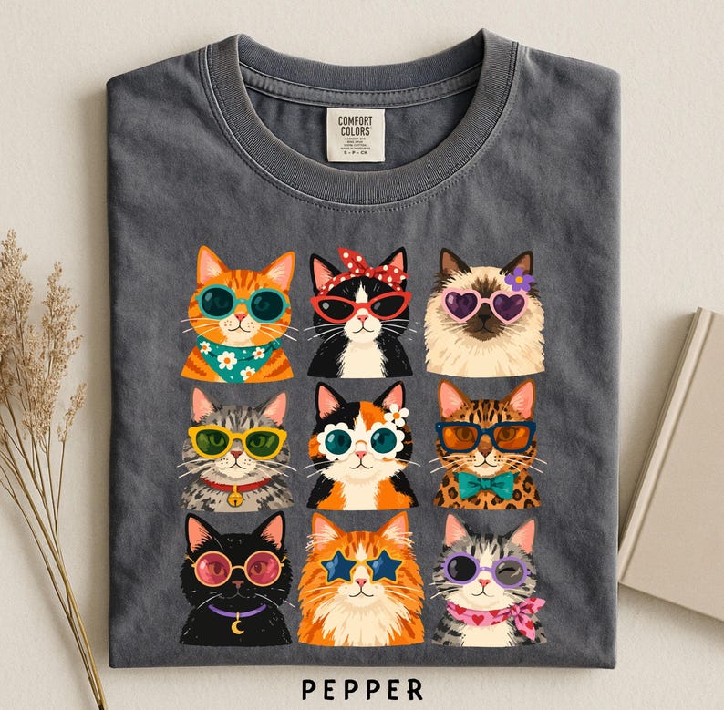 A gray t-shirt with a graphic design of nine cats wearing sunglasses and accessories, arranged in a 3x3 grid.