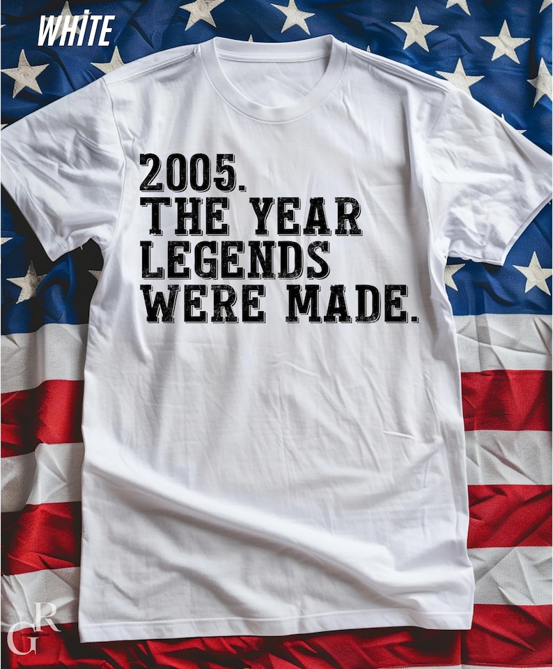 A white t-shirt with the text "2005. THE YEAR LEGENDS WERE MADE." printed on it, placed on top of an American flag.