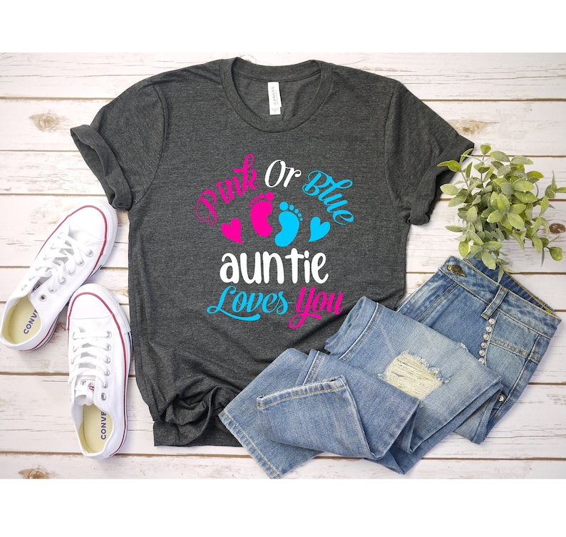 May include: A dark grey t-shirt with the text "Pink or Blue auntie loves you" in pink, blue, and white. The shirt is decorated with pink and blue footprints and hearts.