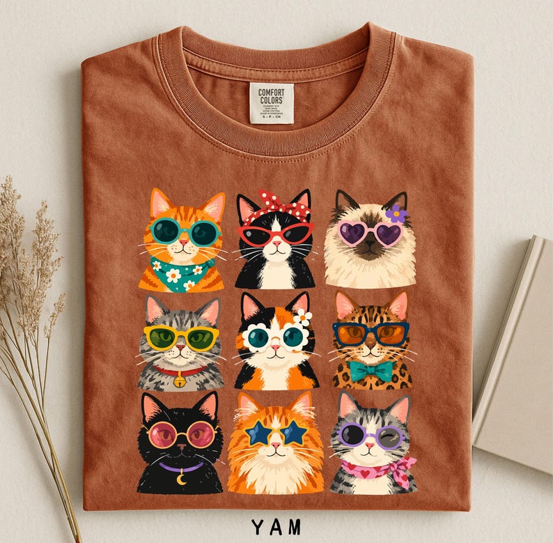 A t-shirt with a collage of nine cat illustrations wearing sunglasses and accessories, arranged in a 3x3 grid.