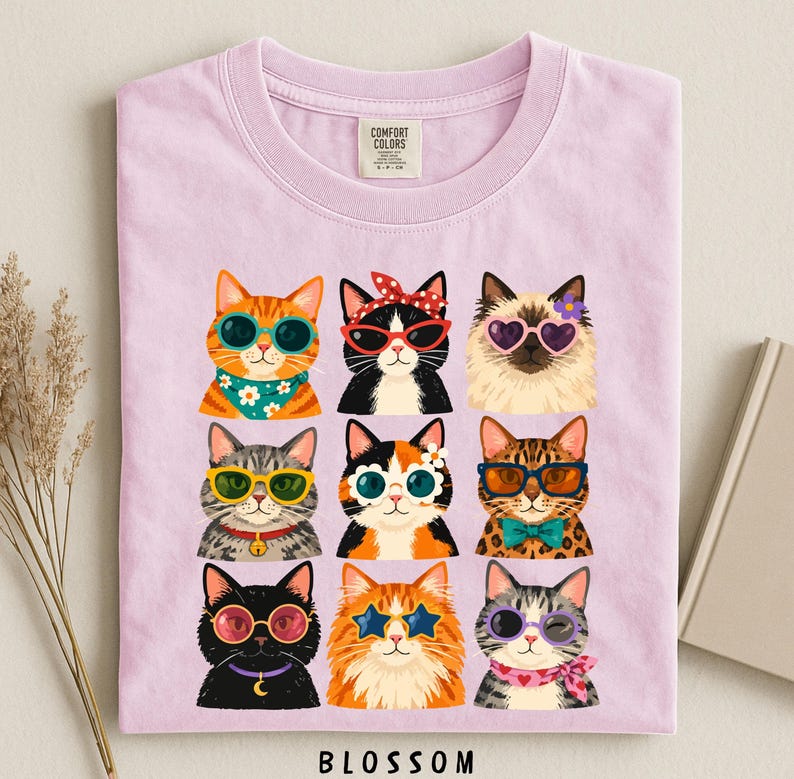 A pink t-shirt with a collage of nine cat illustrations wearing sunglasses and accessories, arranged in a 3x3 grid.