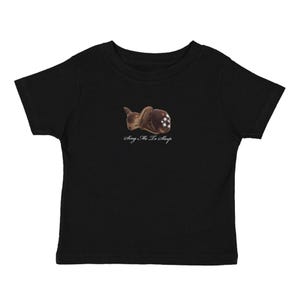 May include: Black toddler t-shirt featuring a brown illustration of a sleeping deer with white spots. The text "Sing Me To Sleep" is printed in a cursive font below the deer graphic. The shirt is made of soft material.