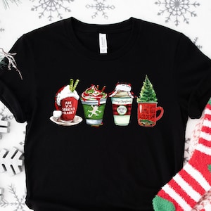 Puede incluir: Camiseta negra con un gr&aacute;fico de cuatro tazas de caf&eacute; con tem&aacute;tica navide&ntilde;a. Las tazas est&aacute;n decoradas con dise&ntilde;os rojos y verdes y tienen texto que dice "Are You Serious Claus?", "Merry Christmas Y'all" y "Little Full Lot Of Sap".