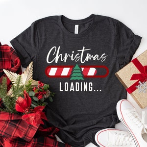 May include: A dark gray t-shirt with a white graphic that says "Christmas Loading..." with a progress bar and a green Christmas tree. The progress bar is red and white striped like a candy cane.