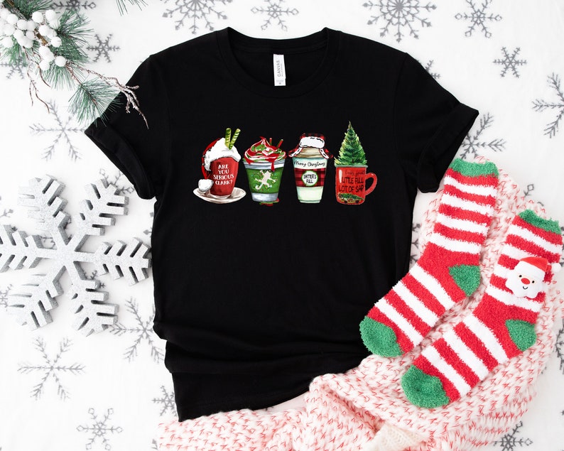 Puede incluir: Camiseta negra con un gr&aacute;fico de cuatro tazas de caf&eacute; con tem&aacute;tica navide&ntilde;a. Las tazas est&aacute;n decoradas con dise&ntilde;os rojos y verdes y tienen texto que dice "Are You Serious Claus?", "Merry Christmas Y'all" y "Little Full Lot Of Sap".