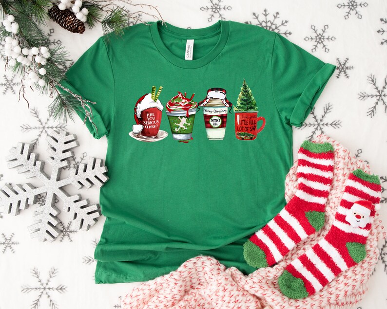 Puede incluir: Camiseta verde con un dise&ntilde;o navide&ntilde;o con cuatro tazas con bebidas festivas y el texto "Are you serious, Clark?"  "Merry Christmas" y "Little bit of sap".