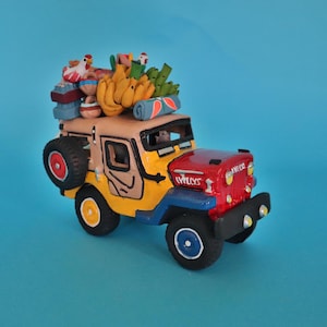 May include: A yellow, red, and blue toy jeep with a driver and a variety of items on the roof, including bananas, a chicken, and a blue blanket.