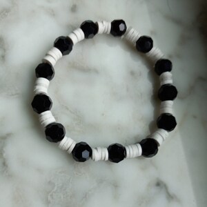 Puede incluir: Un brazalete de cuentas negras y blancas con cuentas negras alternas y separadores blancos.