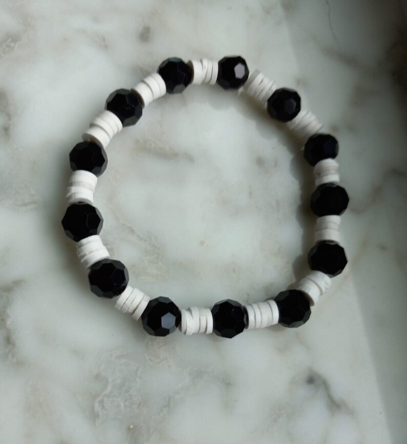 Puede incluir: Un brazalete de cuentas negras y blancas con cuentas negras alternas y separadores blancos.