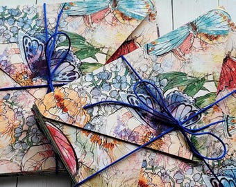 May include: Two decorative paper envelopes with floral and butterfly designs. The envelopes are tied with blue string. The floral pattern includes pink, orange, and blue flowers. The butterflies have blue, red, and white wings.