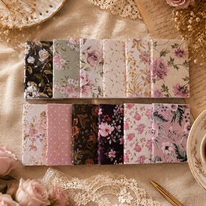 May include: A collection of floral-patterned notebooks in various designs. The notebooks feature a range of colors, including pink, green, and black, with detailed botanical illustrations. The notebooks are arranged on a neutral-toned surface.