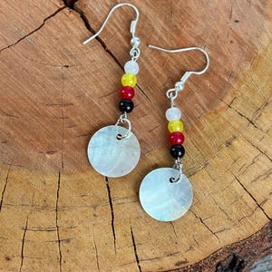 May include: A pair of silver dangle earrings with a white shell disc and a beaded drop featuring black, red, yellow, and white beads.