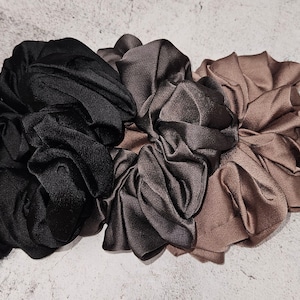 May include: Three fabric scrunchies in black, dark gray, and brown. The scrunchies are made of a soft, silky material and are perfect for holding hair in place.