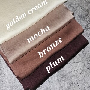 May include: Four fabric swatches in different colors: golden cream, mocha, bronze, and plum. The swatches are stacked on top of each other, with the golden cream swatch on top.