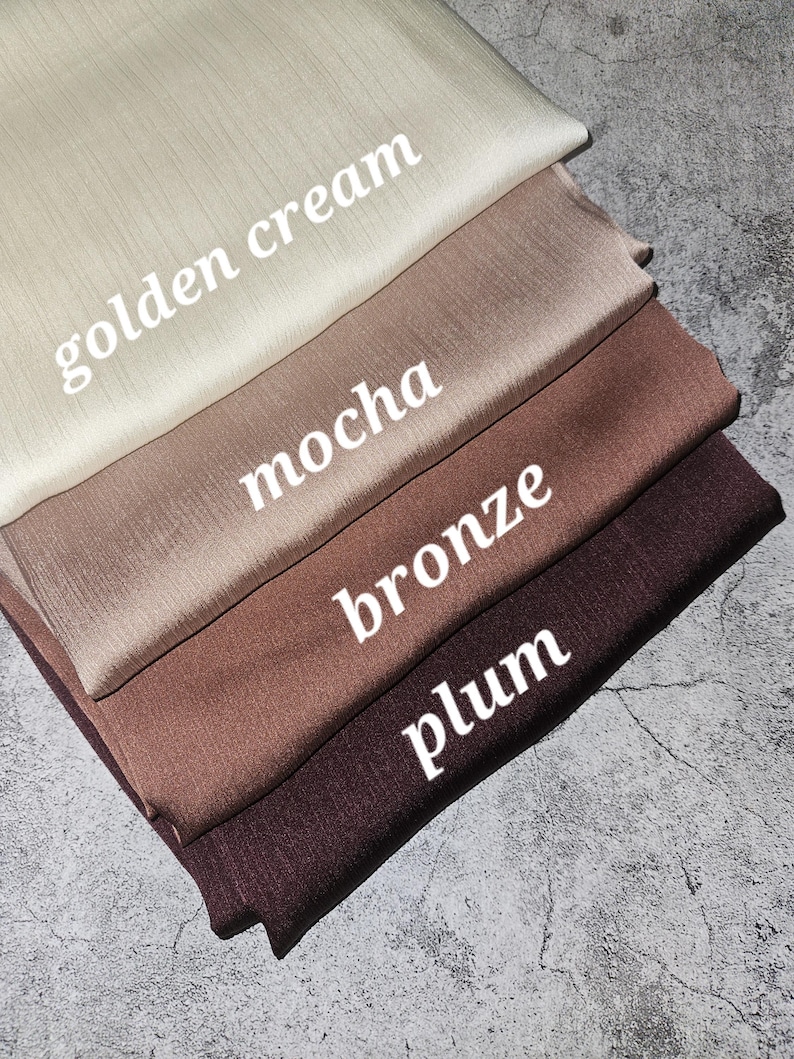 May include: Four fabric swatches in different colors: golden cream, mocha, bronze, and plum. The swatches are stacked on top of each other, with the golden cream swatch on top.