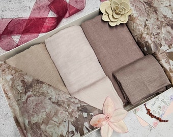May include: A set of five scarves in various shades of brown and pink, arranged in a white gift box with a floral design. The scarves are made of soft fabric and have a delicate texture.