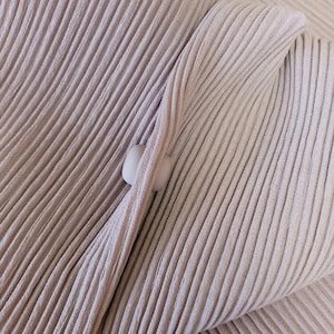 May include: A close-up of a light brown fabric with a ribbed texture. The fabric is folded over itself, creating a soft, rounded shape.