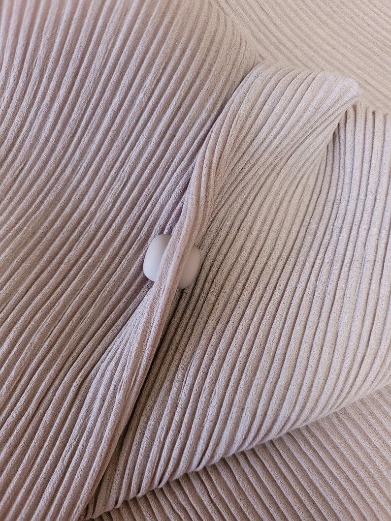 May include: A close-up of a light brown fabric with a ribbed texture. The fabric is folded over itself, creating a soft, rounded shape.
