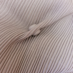 May include: A close-up of a beige fabric with a textured, pleated design. Two white buttons are visible in the center of the image.