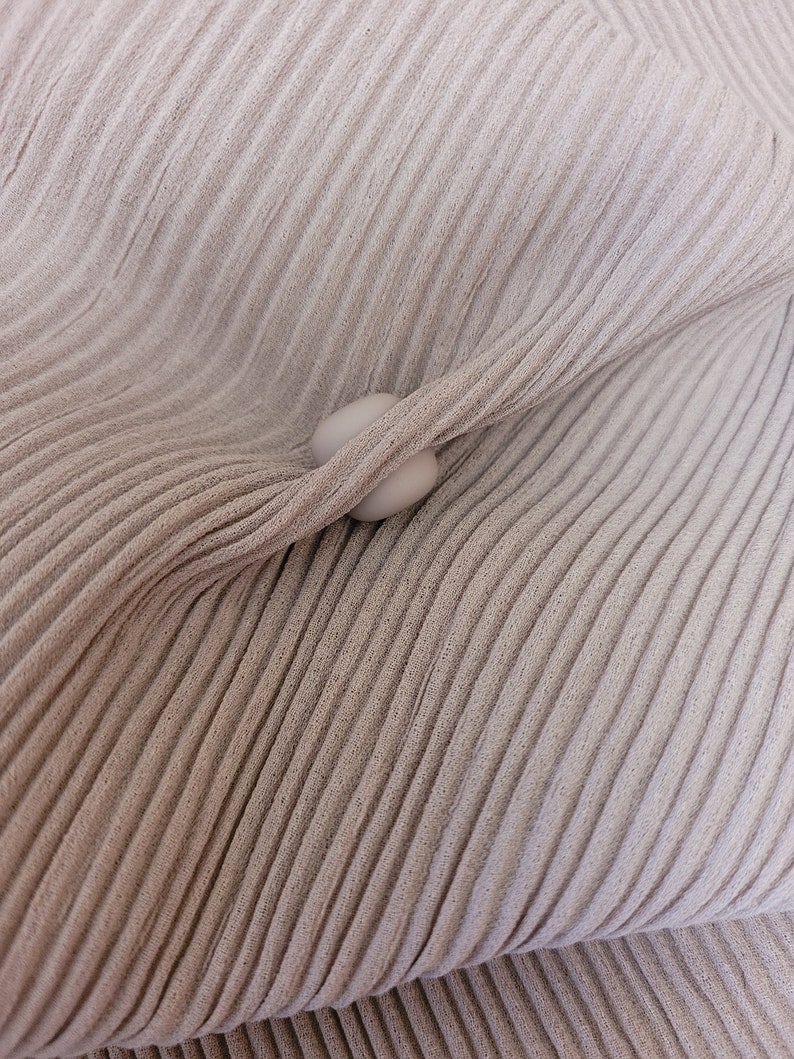 May include: A close-up of a beige fabric with a textured, pleated design. Two white buttons are visible in the center of the image.