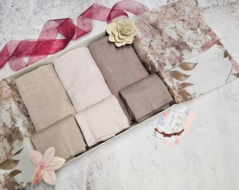 May include: A white gift box with a floral design lid, filled with six soft, beige and pink scarves. The box is tied with a burgundy ribbon and a small white flower.