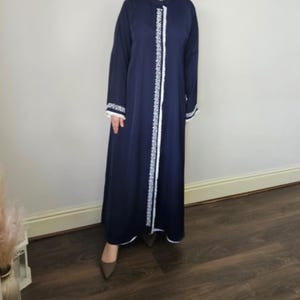 Puede incluir: Una abaya azul marino con ribete de encaje blanco en la parte delantera y en las mangas.