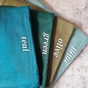 K&ouml;nnte beinhalten: Vier Stoffmuster in verschiedenen Gr&uuml;nt&ouml;nen: Minze, Oliv, Gr&uuml;n und Teal. Die Muster sind in einem Stapel angeordnet, wobei das Minzemuster oben und das Teal-Muster unten liegt.