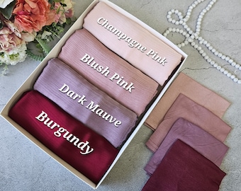 May include: A set of five silk scarves in a white box. The scarves are in shades of pink, mauve, and burgundy. The colors are labeled "Burgundy", "Dark Mauve", "Blush Pink", and "Champagne Pink".