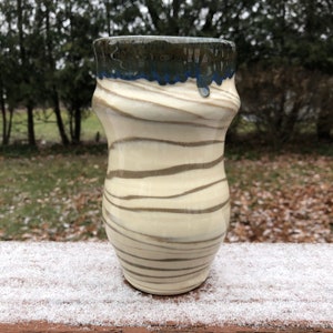 Può includere: Un vaso in ceramica bianca con smalto marrone e blu. Il vaso ha una forma ondulata, organica e una bocca larga.
