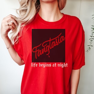 May include: Red t-shirt with a black square graphic that says "Fangtasia" in red cursive lettering. The text below the graphic says "life begins at night" in white lettering.