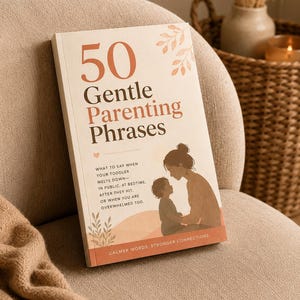 Puede incluir: Un libro titulado "50 Gentle Parenting Phrases" con una cubierta blanda. La portada presenta texto e ilustraciones de una madre y un niño. El libro está sobre un sillón beige con una cesta tejida y una vela en el fondo.