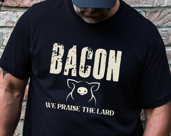 May include: Black t-shirt with a white graphic that says "Bacon" with a pig illustration and the text "We Praise The Lard".