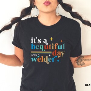 May include: Black t-shirt with a colorful graphic that reads "it's a beautiful day to be a welder".