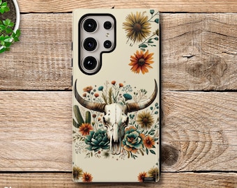 May include: A phone case with a white background and a floral design featuring a skull with horns. The flowers are in shades of orange, yellow, green, and blue.
