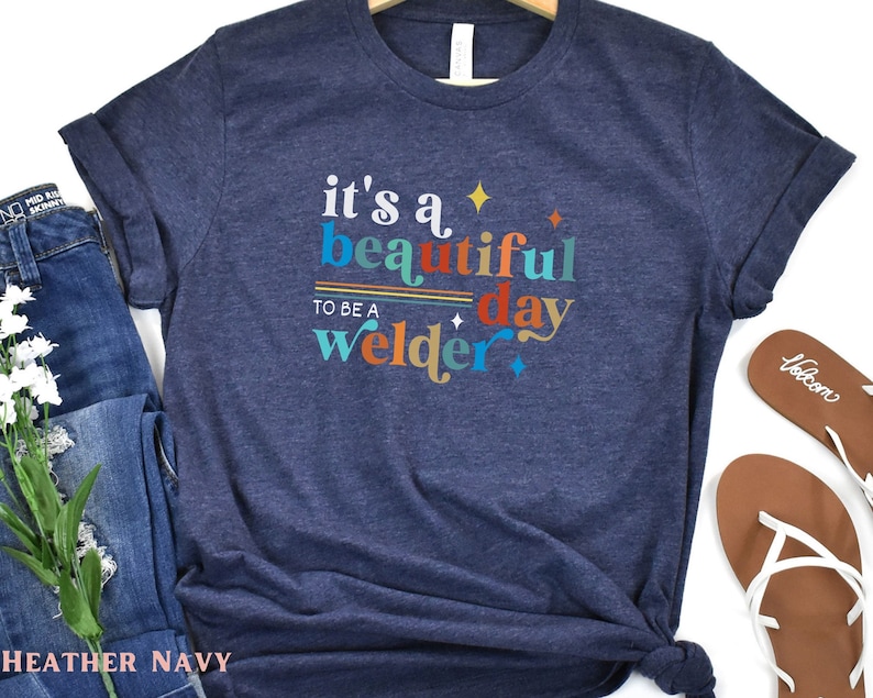 May include: A heather navy blue t-shirt with the text "it's a beautiful day to be a welder" in colorful retro lettering.