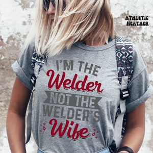 K&ouml;nnte beinhalten: Graues T-Shirt mit dem Text "I'm the Welder not the Welder's Wife" in rot und grau.