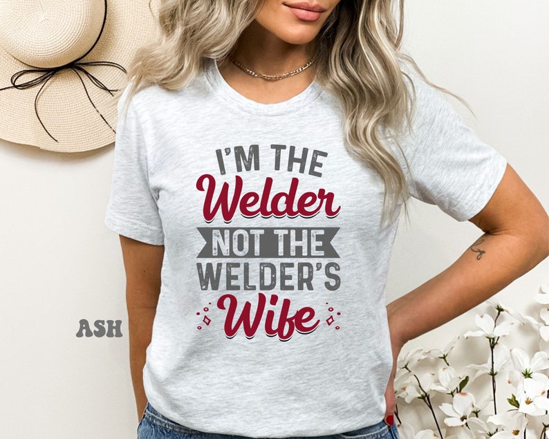 K&ouml;nnte beinhalten: Ein graues T-Shirt mit dem Text "I'm the Welder not the Welder's Wife" in roten Buchstaben.