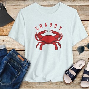 May include: A light blue t-shirt with a red crab illustration and the word "CRABBY" in white letters.
