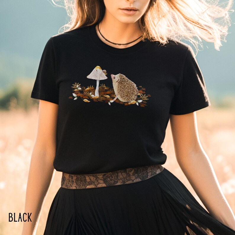 Puede incluir: Camiseta negra con una imagen bordada de un erizo mirando un hongo.