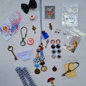 Puede incluir: Accesorios para muñecas con temática de Alicia en el País de las Maravillas, que incluyen un vestido blanco, medias blancas y negras, un lazo negro, una llave, una botella, un hongo y una variedad de dijes y adornos.