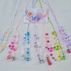 May include: A collection of colorful beaded pullstrings for Blythe dolls. Each string features heart-shaped beads, small charms, and a miniature glass globe filled with glitter. The color palette includes pinks, blues, greens, and purples.