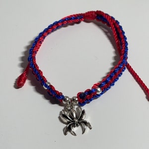 May include: Red and blue braided bracelet with a silver spider charm.