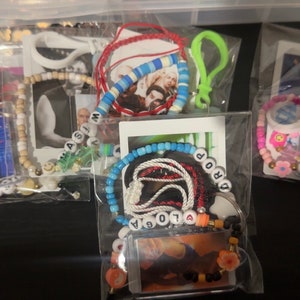 May include: Several clear plastic bags containing handmade jewelry and accessories. The bags hold bracelets, necklaces, and keychains with beads, charms, and photos. Some items have names spelled out with letter beads.